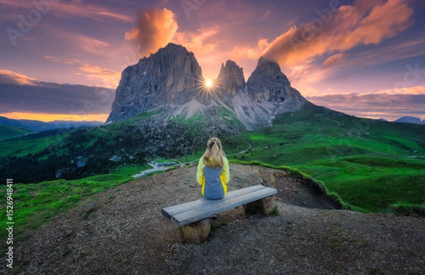 Obraz Girl is sitting on the wooden bench on mountain peak in beautiful alpine mountains at sunrise in summer. Landscape with young woman in alps, high rocks, colorful sky with clouds. Dolomites, Italy
