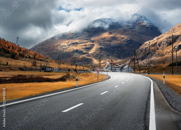 Obraz Empty asphalt road winding through alpine mountains in clouds at sunset in autumn. Landscape with majestic Alps, orange trees and grass, dramatic cloudy sky in fall. Road on mountain pass. Switzerland