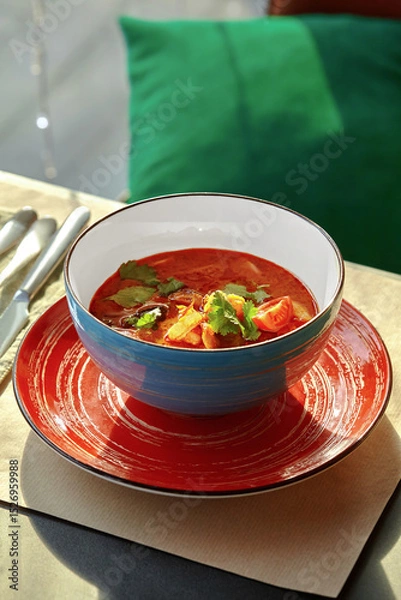 Fototapeta Tom yum soup served in blue bowl on red plate with cutlery aside
