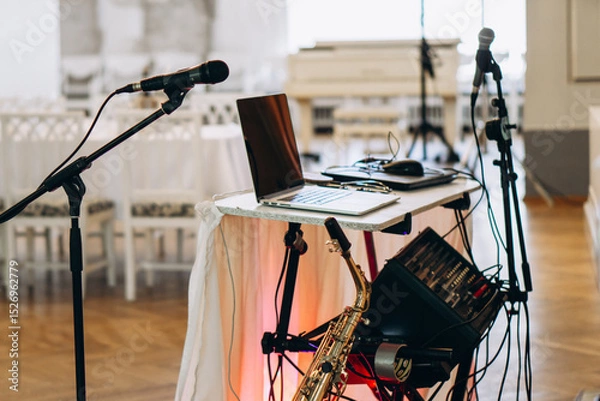 Fototapeta Elegant music setup with laptop, saxophone, and microphones prepared for a live performance in a sophisticated event venue wedding DJ musician