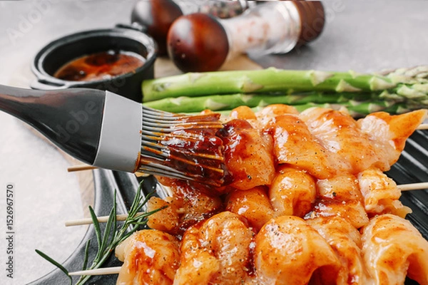Fototapeta Brush with marinade sauce for marinating kebabs. Raw chicken breast kebab. Raw sliced chicken breast on wooden sticks with asparagus