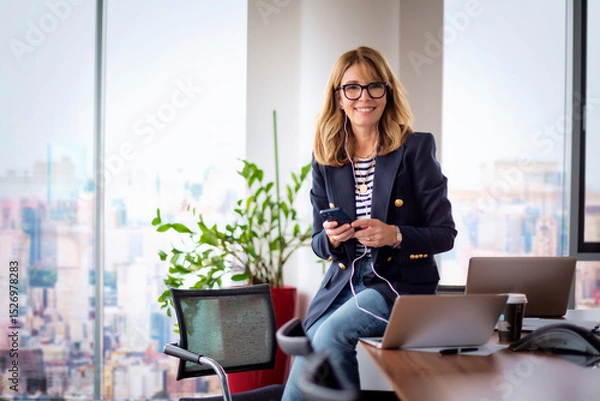 Obraz Blond haired business woman using a laptop and smart phone in a modern office