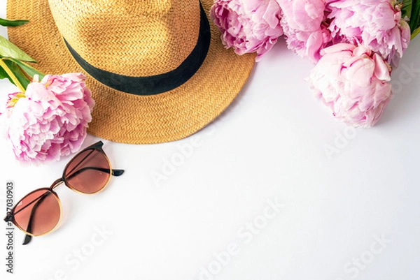 Fototapeta Straw hat, sunglasses and pink peonies arranged on white background, top view summer fashion concept. Flat lay, copy space