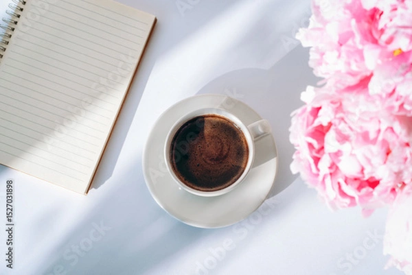 Fototapeta A cup of coffee, notepad and peony flowers on white background with shadows. Top view