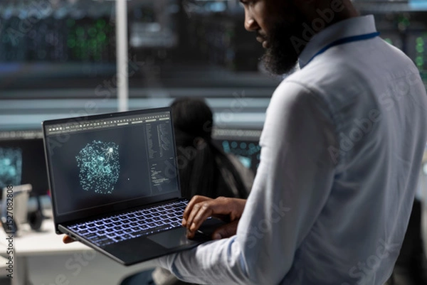 Fototapeta Data center engineer uses AI visualization tool on laptop to optimize resource allocation. Server hub IT expert uses artificial intelligence analysis on notebook to do maintenance