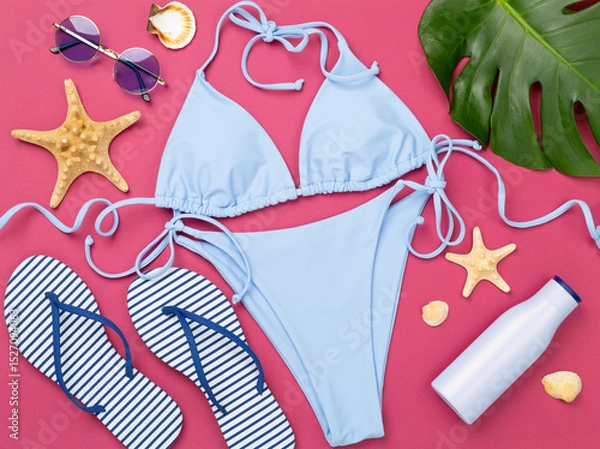 Fototapeta Blue bikini with beach accessories on color background, top view