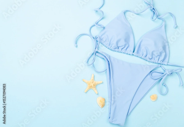 Fototapeta Blue bikini with beach accessories on color background, top view