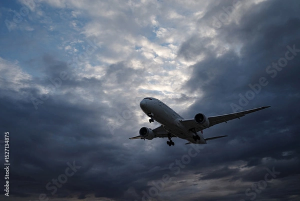 Obraz 曇り空の早朝、着陸態勢で上空を飛んでいく飛行機