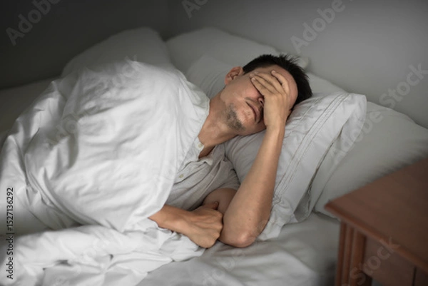 Fototapeta Sleepless man lying in bed feeling tired exhausted stressed waking up unmotivated 