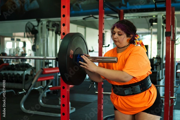 Fototapeta View of an overweight young Latina woman carrying weights and preparing to workout at a gym. Pushing herself. Improvement and well-being.