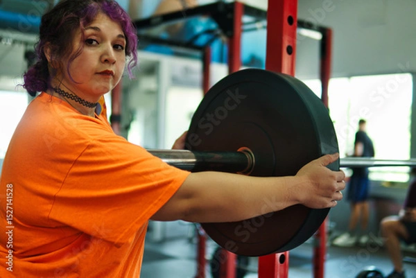 Fototapeta View of an overweight young Latina woman carrying weights and preparing to workout at a gym. Pushing herself. Improvement and well-being.