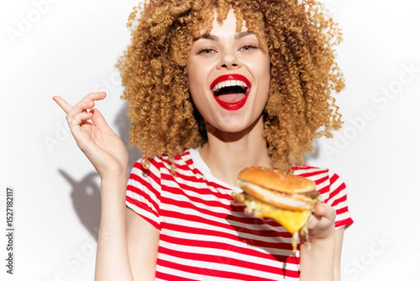 Fototapeta Cheerful woman with curly hair holding a burger, expressing joy and excitement, on a bright white background Perfect for healthy eating concepts
