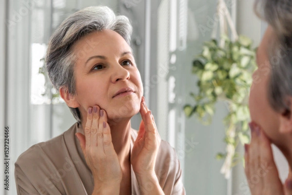 Fototapeta Smiling elderly woman of the age of a pensioner iwith gray hair does herself a manual facial massage