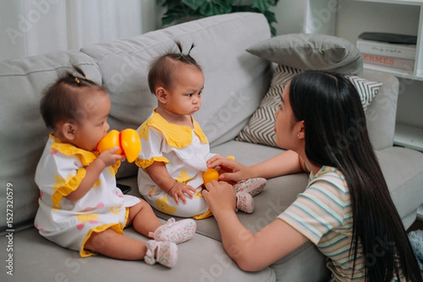 Obraz Portrait of Single mother spends happy time with her twin daughters in a warm room at home. Take care of baby with love and care.