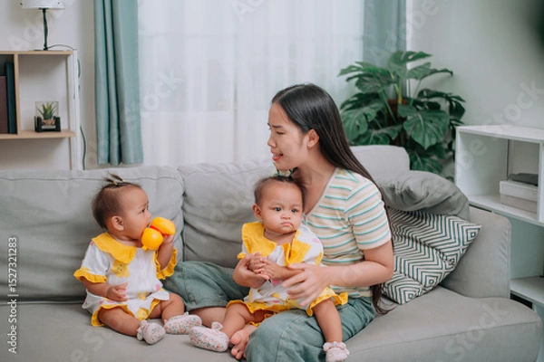 Obraz Portrait of Single mother spends happy time with her twin daughters in a warm room at home. Take care of baby with love and care.