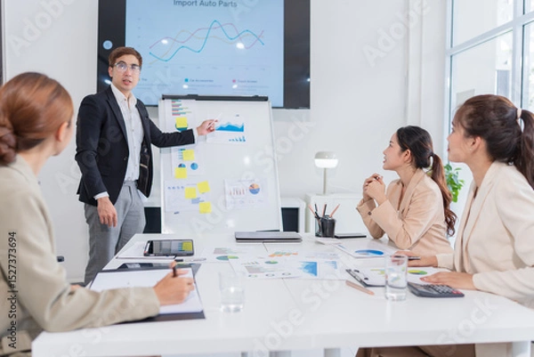 Fototapeta Group of Asian business people present their work on a table with graph paper.