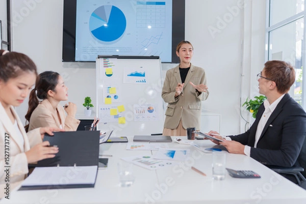 Fototapeta Group of Asian business people present their work on a table with graph paper.