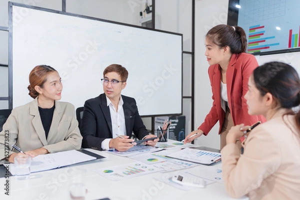 Fototapeta Group of Asian businesspeople sit at a table with graph paper in a meeting.