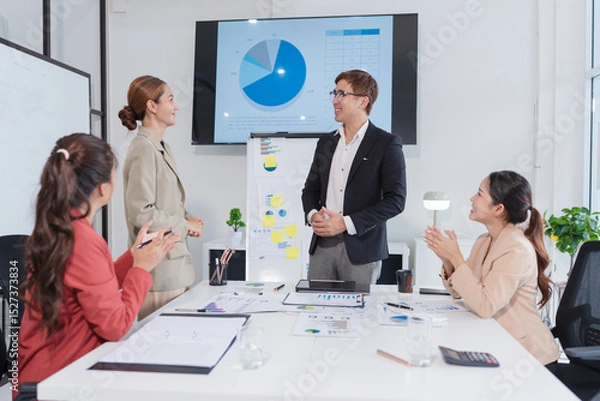 Fototapeta Group of Asian businesspeople sit at a table with graph paper in a meeting.
