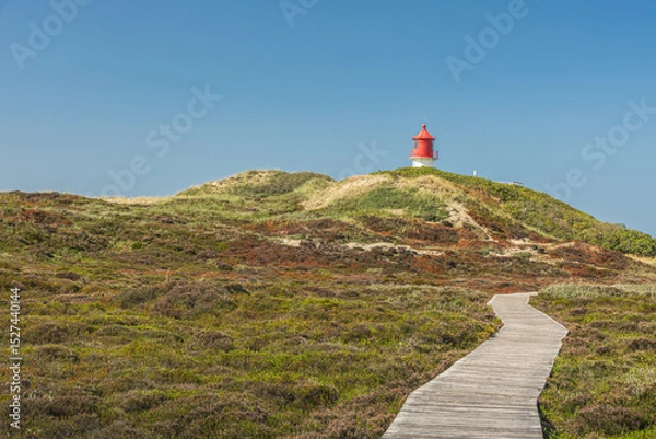 Fototapeta Wooden plank path through the dune landscape of Amrum, with the Quermarkenfeuer lighthouse in the background, Amrum, North Sea, North Frisian Islands, Schleswig-Holstein, Germany