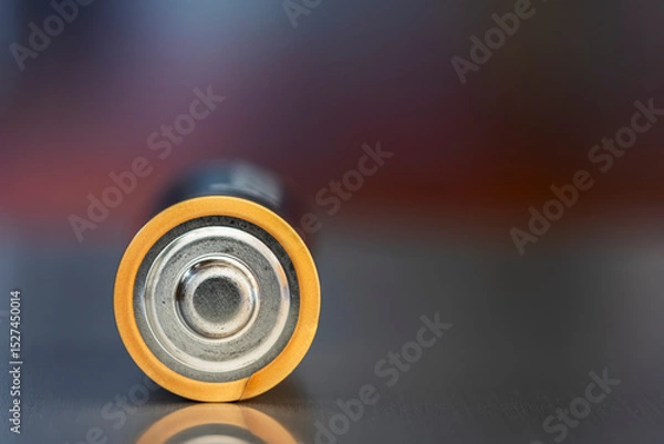 Obraz One AA alkaline battery lies on a metal surface, against a blurred background