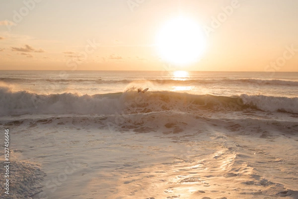 Fototapeta Surfer makes maneuvers and a bottom turn on a wave against the background of the setting sun. A surfer actively rides big waves in the ocean