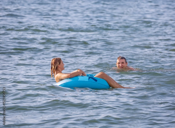 Fototapeta A guy swims up to a young girl floating on an inflatable circle