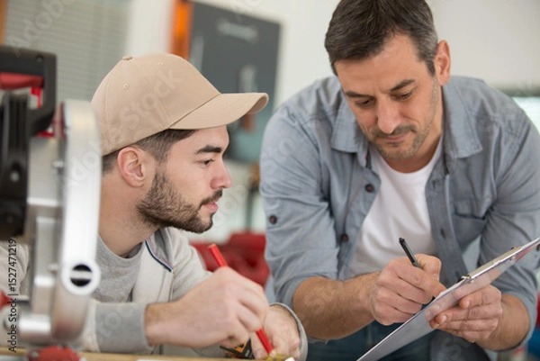 Fototapeta side view portrait of mature carpenter helping young worker