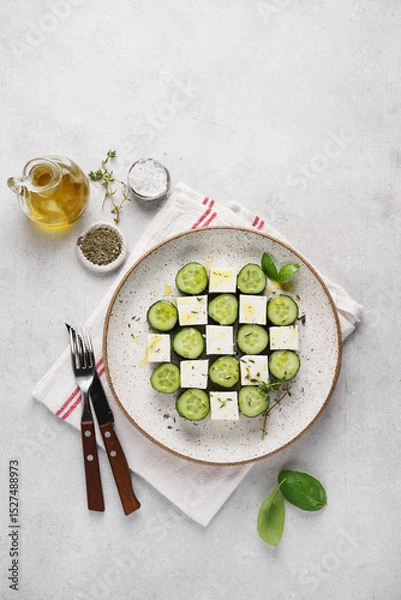 Obraz Stylish serving of cucumber and feta cheese salad on ceramic plate on napkin on white background. vegetarian cuisine. top view