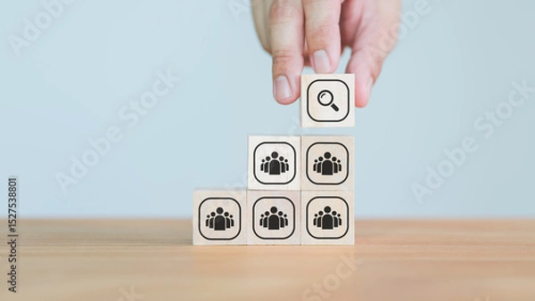 Fototapeta Hand placing a magnifying glass icon wooden cube block above people group wood blocks, representing talent search, company, leadership, recruitment, or leadership selection strategy.