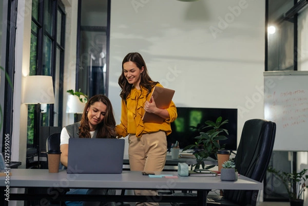 Fototapeta Two gen z female colleagues working together in a modern office