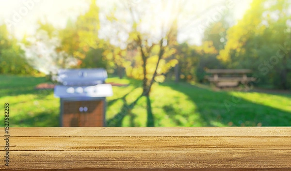 Fototapeta summer time in backyard garden with grill BBQ, wooden table, blurred background