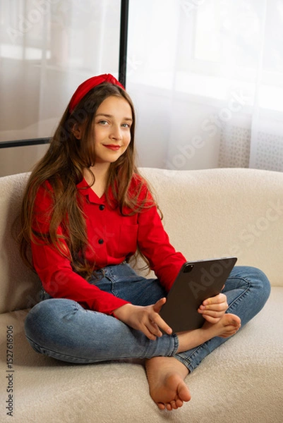 Fototapeta Portrait of smiling teen girl holding tablet on sofa. Concept of lifestyle, use digital technology