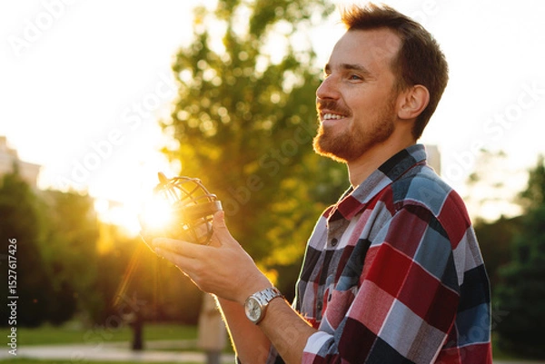 Fototapeta Smiling young man holding globe illuminated by golden sunset. Astronomer holds an armillary sphere outside during an open class on spherical astronomy