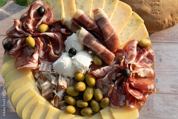 Fototapeta Catering on a wooden board on a rustic table, meat, olives, cheese, and a drink as an appetizer