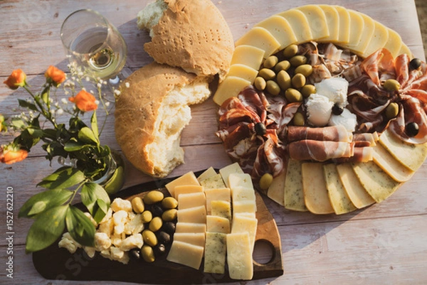 Fototapeta Catering on a wooden board on a rustic table, meat, olives, cheese, and a drink as an appetizer