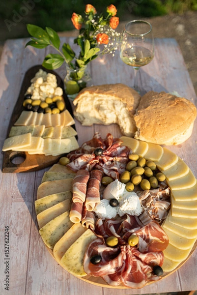 Fototapeta Catering on a wooden board on a rustic table, meat, olives, cheese, and a drink as an appetizer