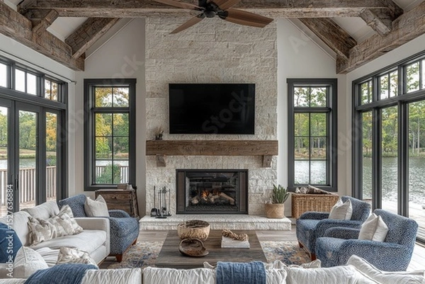 Fototapeta Modern family room with white oak stone fireplace, light blue and navy patterned armchairs, grey sofa, dark wood coffee table, rustic ceiling fan, and wall-mounted TV.