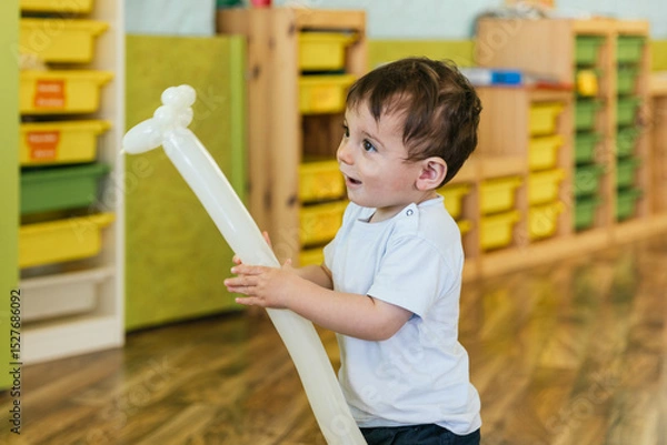 Fototapeta Happy toddler boy playing with giraffe balloon in kindergarten