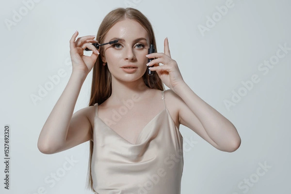 Fototapeta Woman applying mascara in a stylish setting with soft lighting showcasing beauty