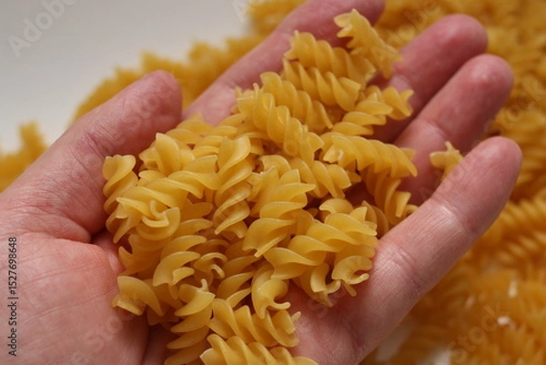 Obraz A handful of dry pasta in hand on a blurred background. Selective focus.