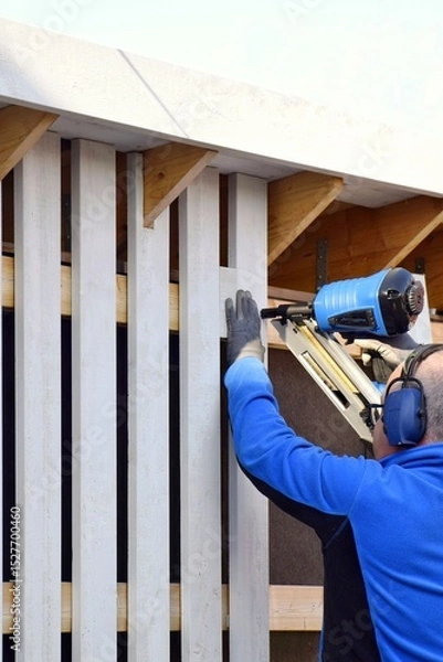 Obraz Man using pneumatic stapler, nail gun for wooden board, driving metal nails and staples.