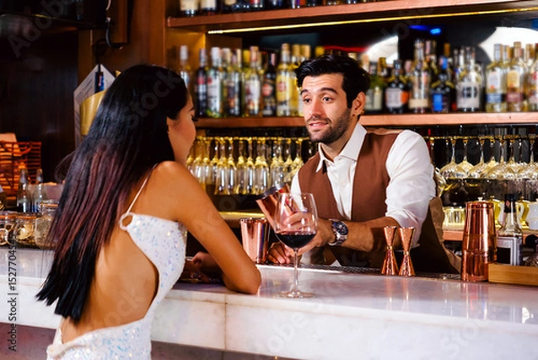 Fototapeta Bartender serves red wine to a woman in a glamorous dress at a vibrant nightclub bar, capturing nightlife service, hospitality, and customer interaction in a luxury drinking environment.