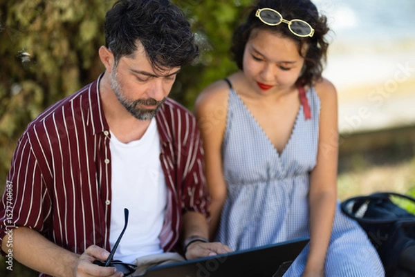 Fototapeta Couple enjoying a relaxed outdoor reading session together, sitting comfortably with a book in a peaceful park setting on a sunny day