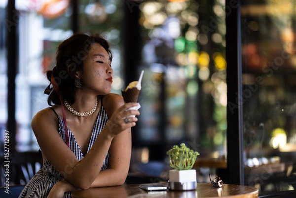 Fototapeta Woman enjoying an ice cream cone in a cafe while relaxing in casual summer attire with a serene expression