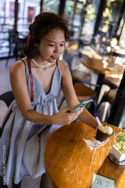 Fototapeta Woman enjoying ice cream in a modern cafe while browsing her phone, capturing a moment of relaxation and leisure time in a stylish setting