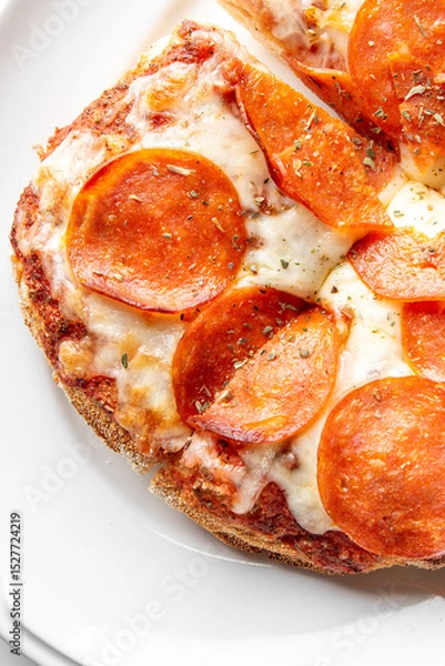 Fototapeta Close-up of a freshly baked pepperoni pizza slice with melted mozzarella cheese, sprinkled with herbs, served on a white plate. The crispy crust and rich tomato sauce enhance its appetizing appearance