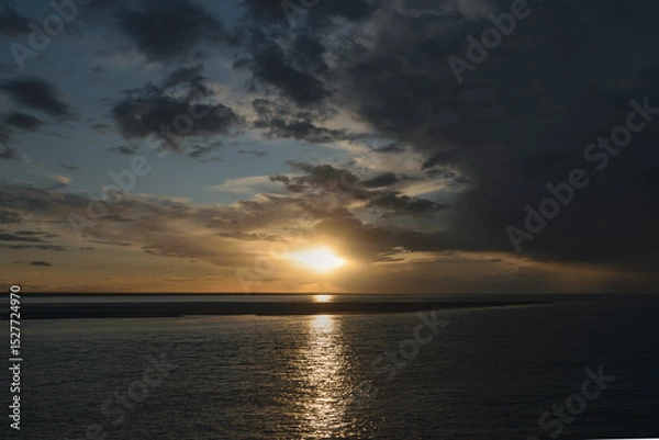 Fototapeta Sunset over calm waters with clouds reflecting favorite hues in a coastal view