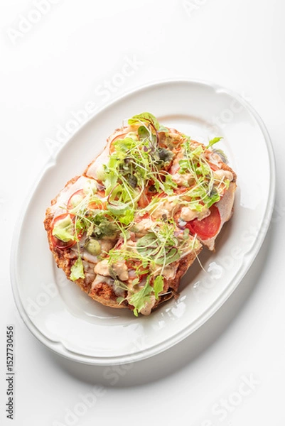 Fototapeta A golden, crispy Roman-style pinsa with a light, airy crust, topped with fresh greens, sliced tomatoes, melted cheese, and creamy dressing, served on a white plate for a delicious meal.
