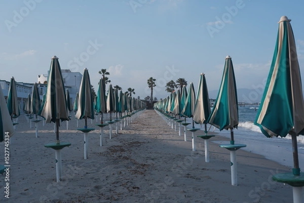 Obraz Closed umbrellas on sandy beach in Sardinia, Poetto shore with summer mood and calm coastal atmosphere